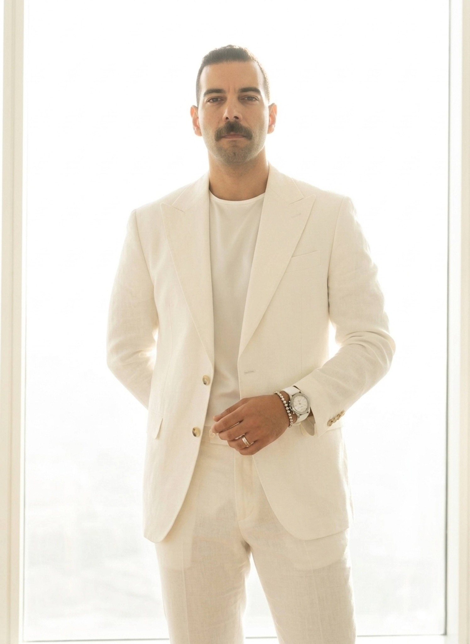 Person in all-white linen suit standing with hands behind back against overexposed bright window
