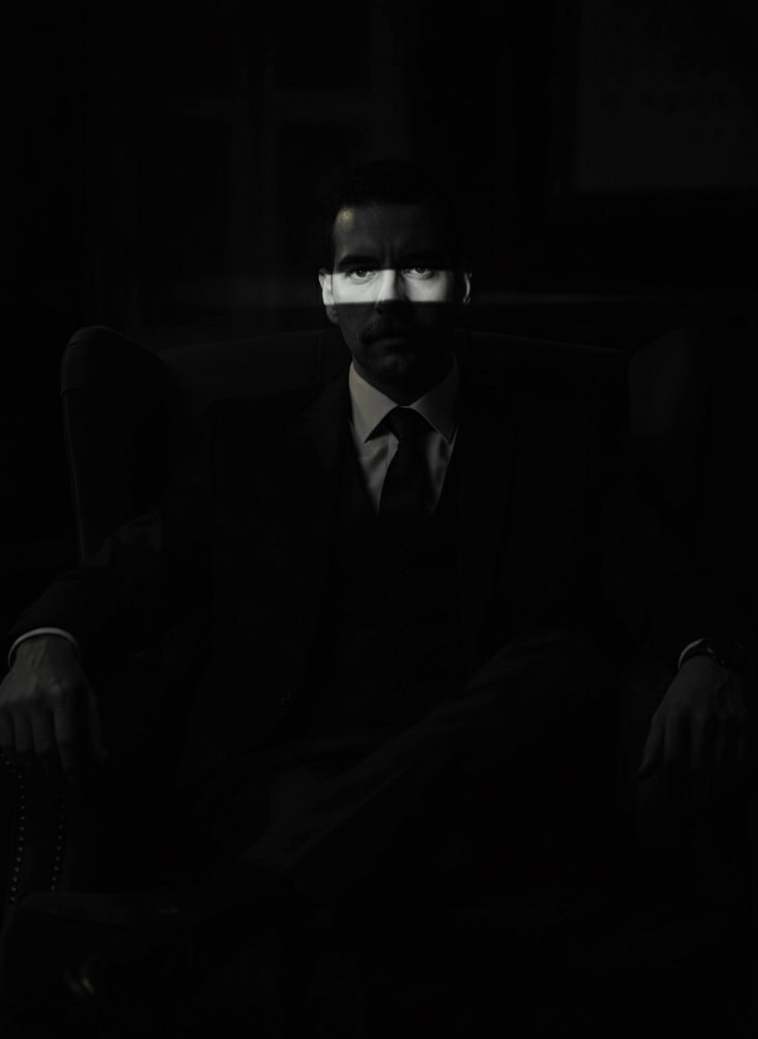 Person motionless in pitch black with thin strip of light across eyes in noir interrogation style