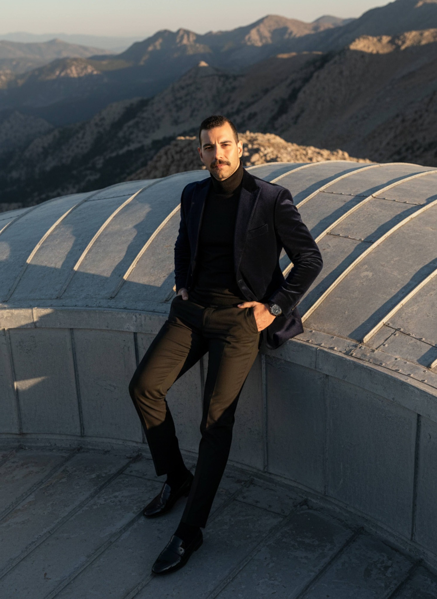Person in navy velvet jacket standing on sun-bleached observatory dome in Pyrenees at sunset