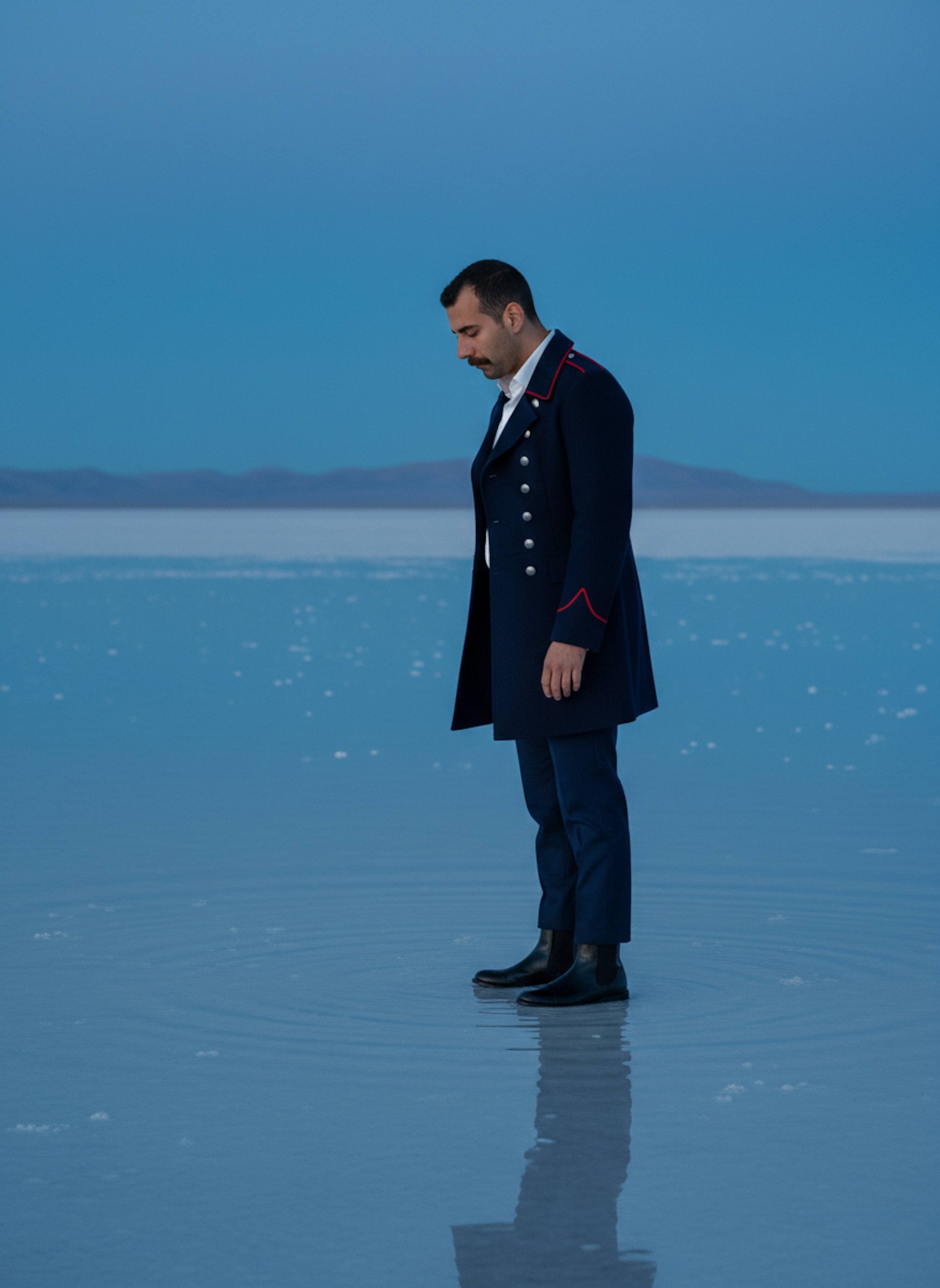 Person in navy officer coat on mirror-like Utah salt flat during blue hour twilight