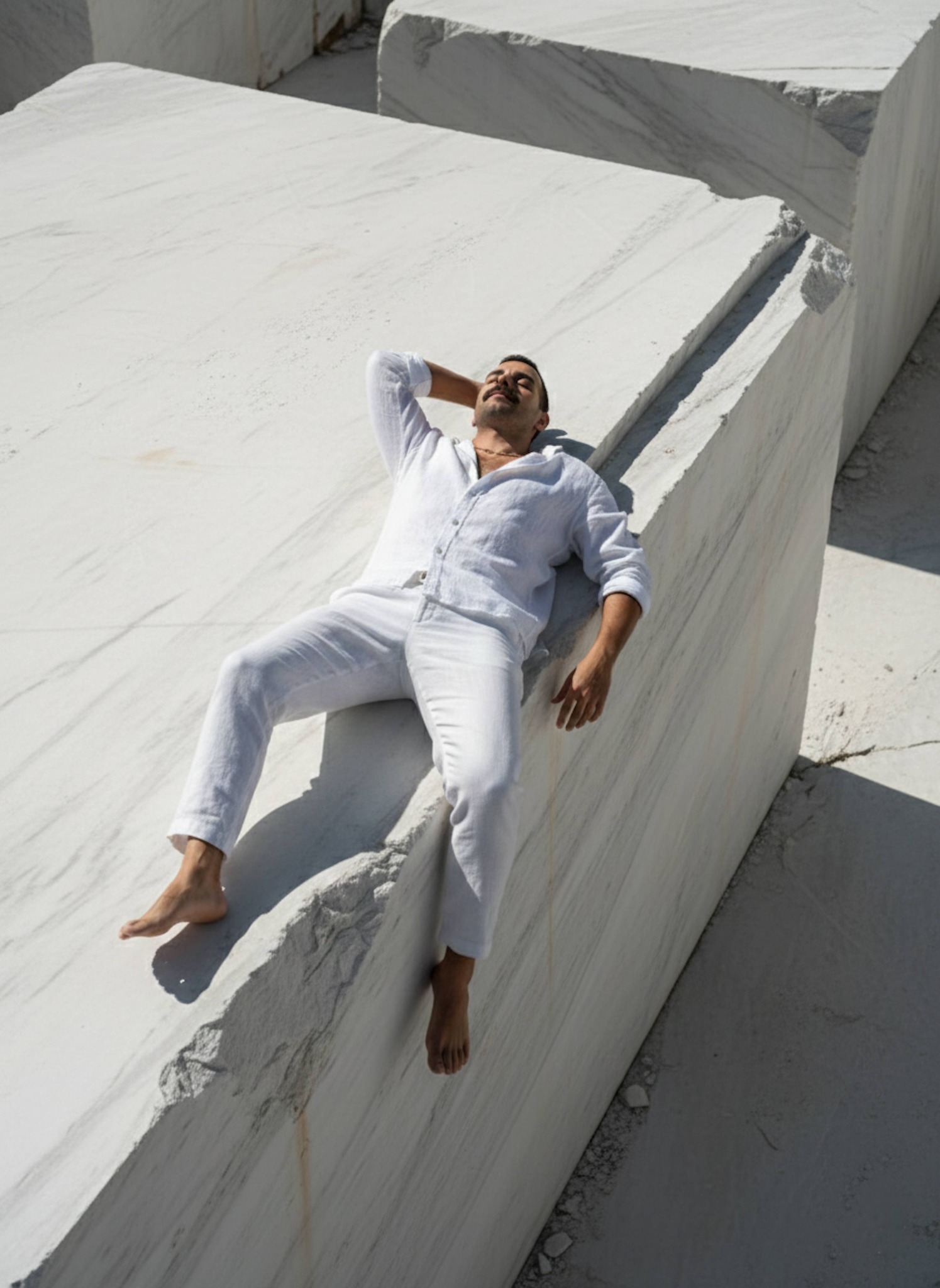 Person in white linen shirt barefoot on sun-drenched Greek marble quarry stones