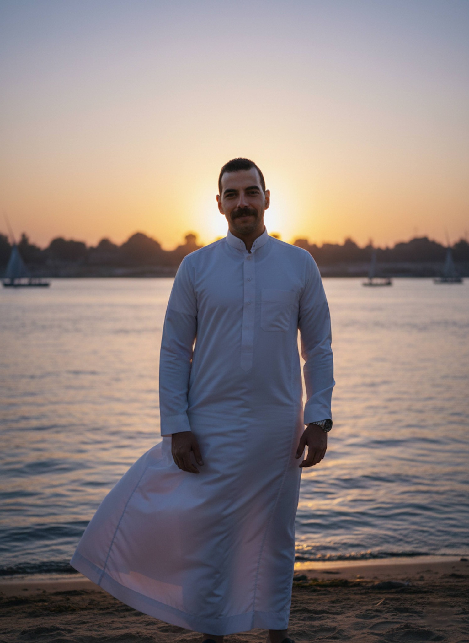 Person in white galabeya standing on Nile riverbank at sunset on last day of Ramadan with golden light and wind