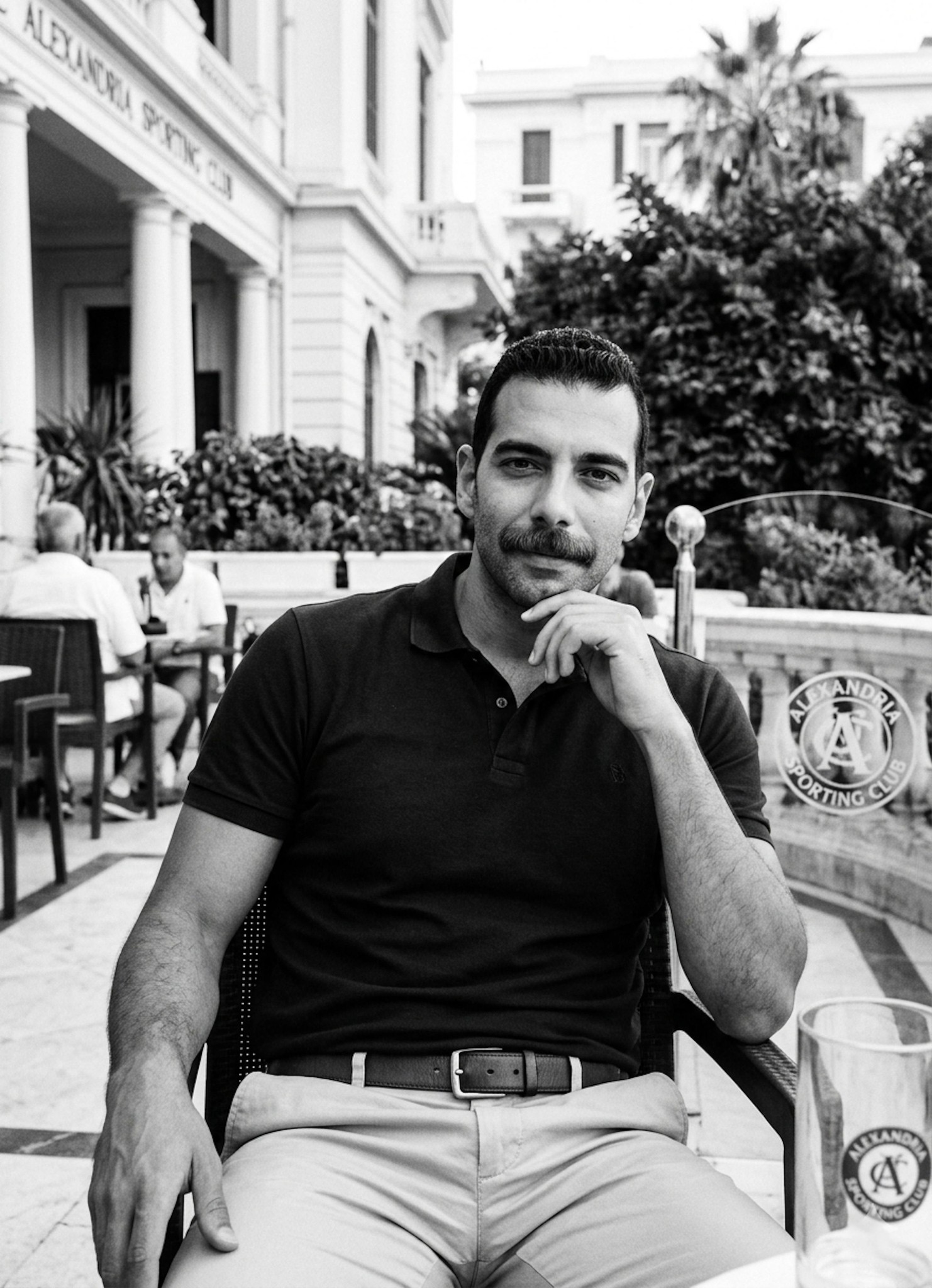 Person in a premium polo shirt and chinos at the Alexandria Sporting Club in a luxury black-and-white lifestyle portrait