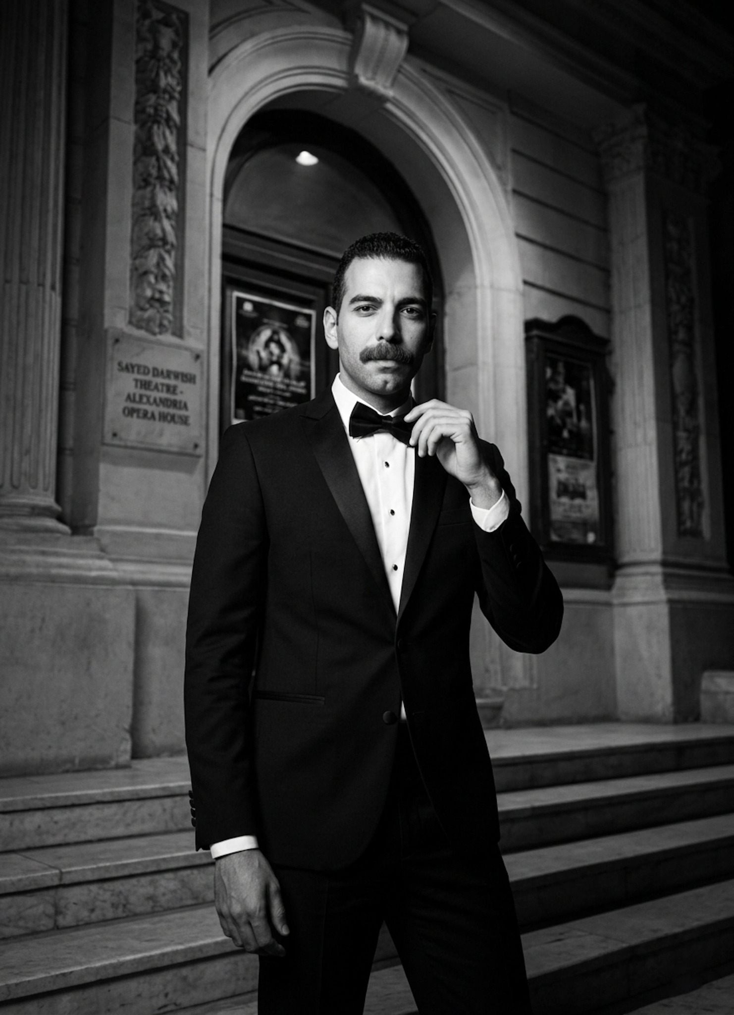 Person in a sharp formal evening suit near the Alexandria Opera House with dramatic theatrical lighting in elegant monochrome