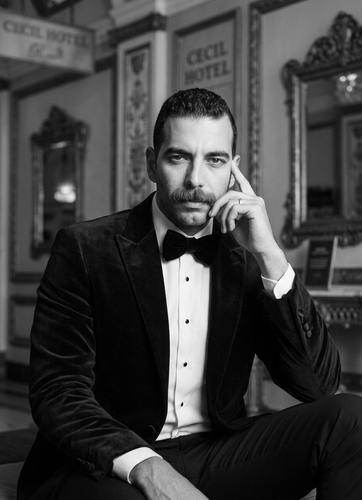 Person in velvet dinner jacket and bowtie inside historic Cecil Hotel with low-key monochrome lighting highlighting fabric texture