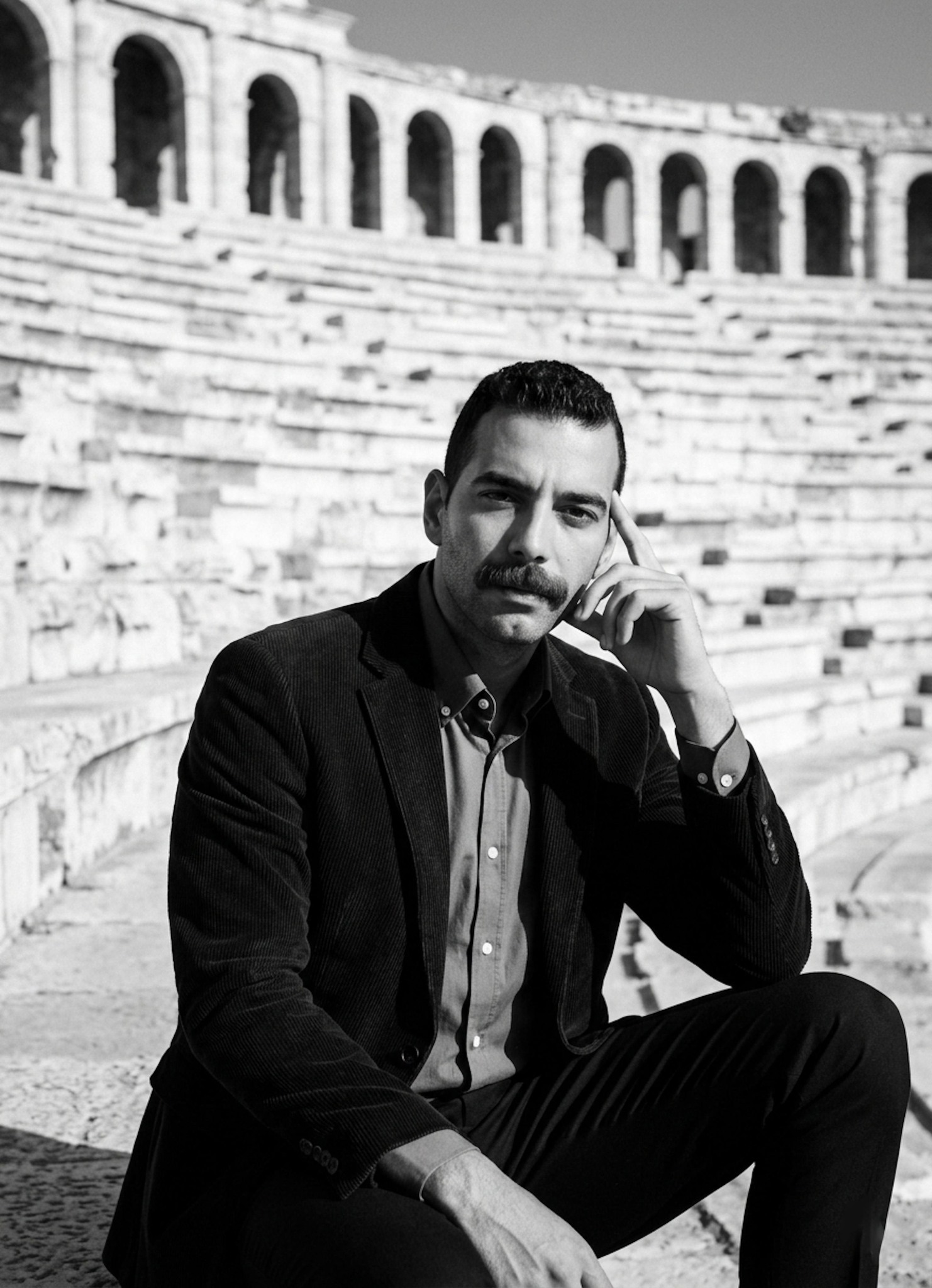 Person in corduroy blazer at Roman Amphitheatre with repetitive stone tiers creating geometric background in black and white