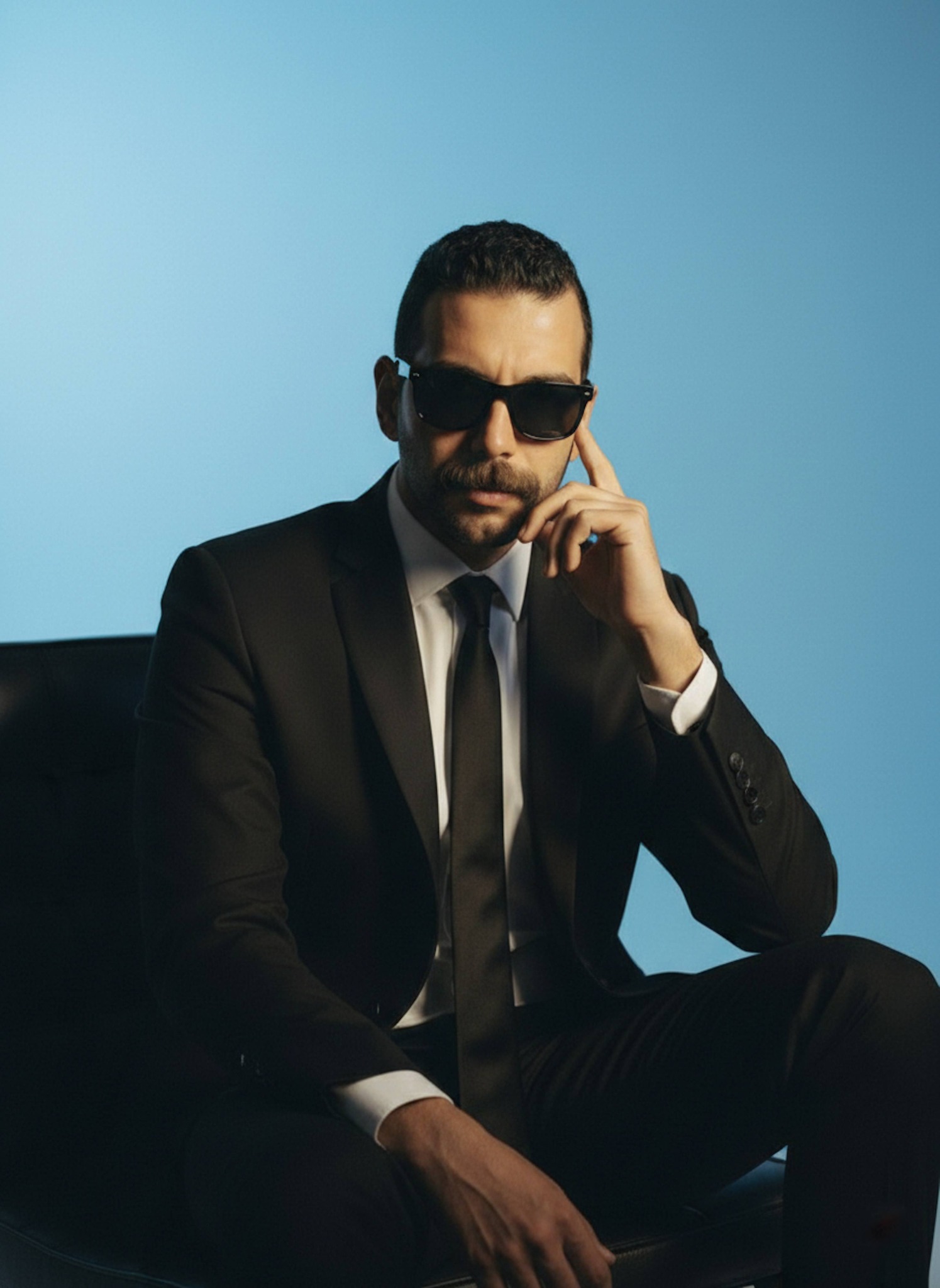Executive in black wool suit and sunglasses seated in a minimalist studio with icy blue gradient backdrop