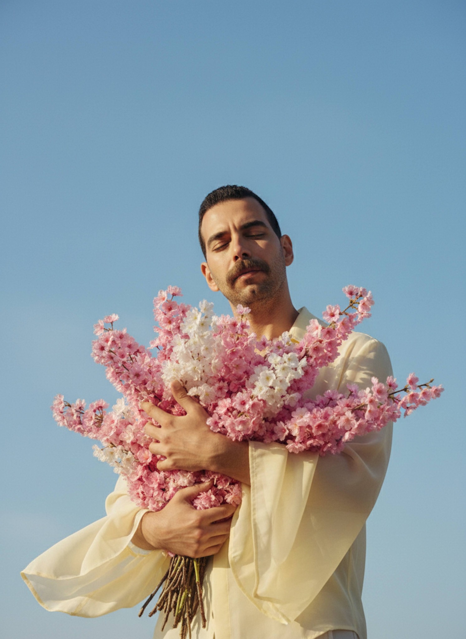 Dreamy portrait of a person holding sakura flowers under blue sky with golden sunlight and closed eyes