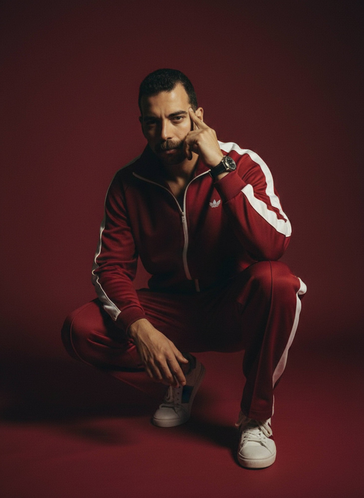 Gritty studio portrait of a person squatting in a vintage red and white tracksuit with dramatic lighting