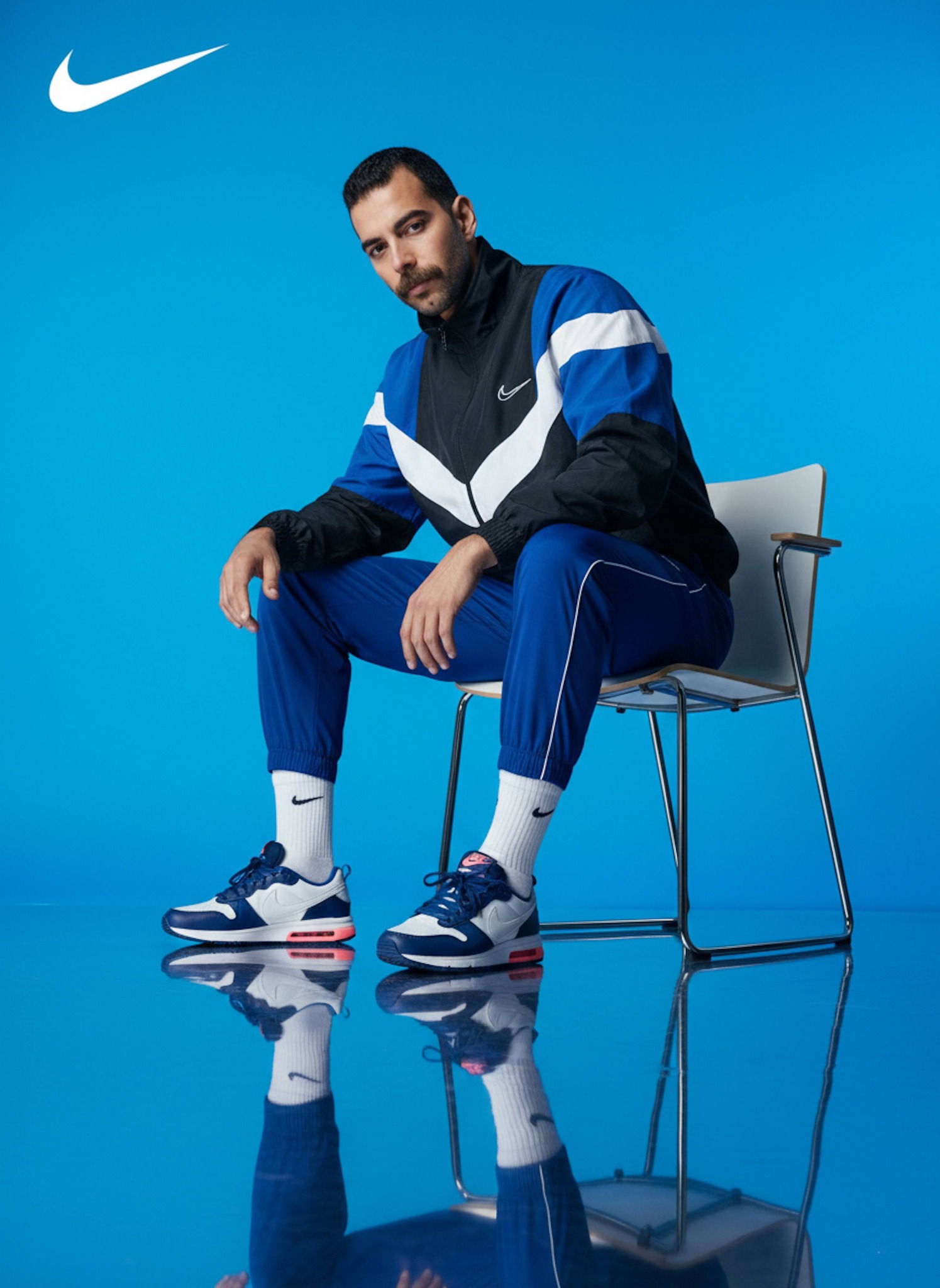 Studio portrait of a person posed sideways in a chair wearing a black and white retro tracksuit