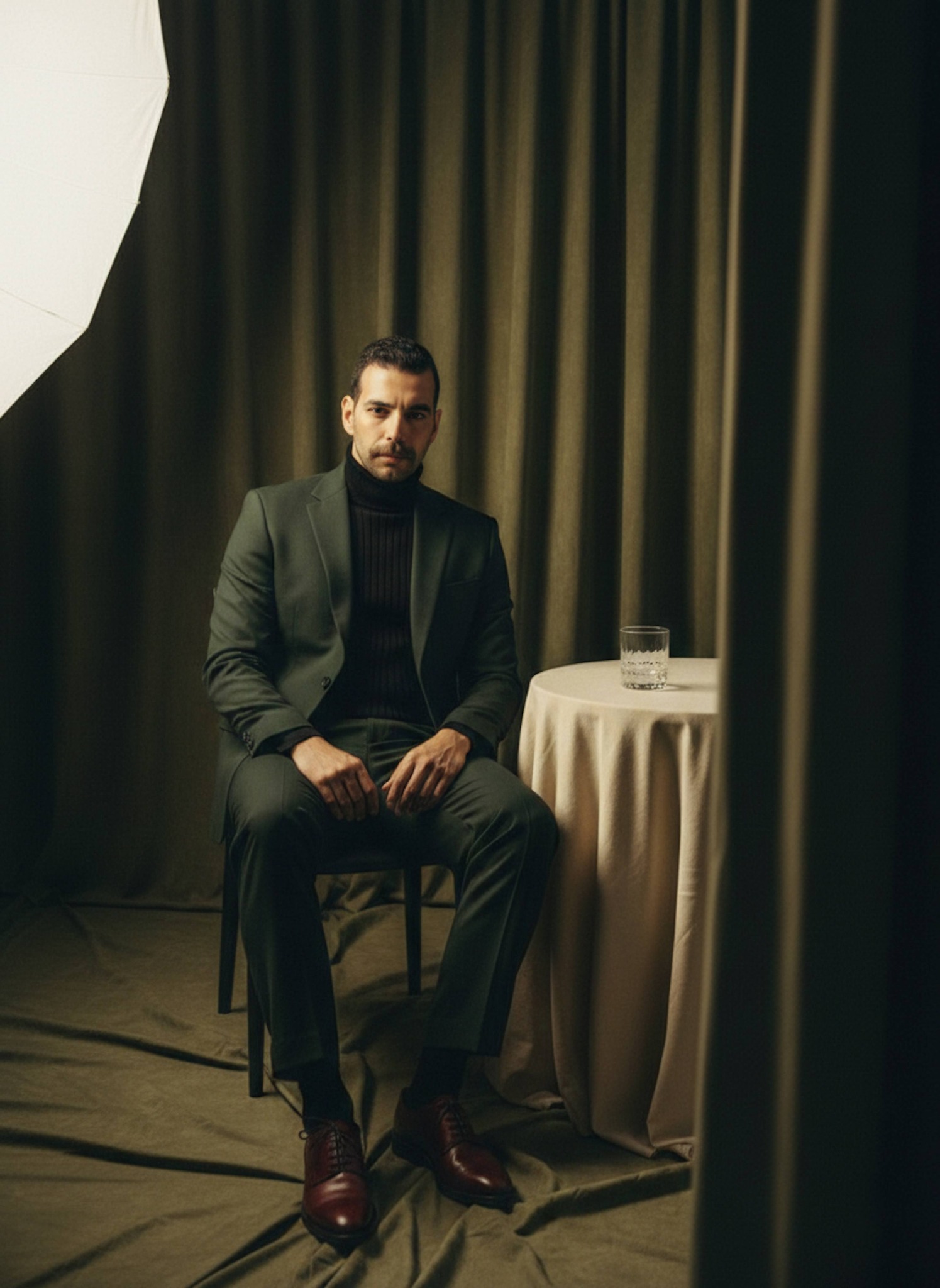 Cinematic portrait of a person in a deep green wool suit and black turtleneck in an olive-toned studio
